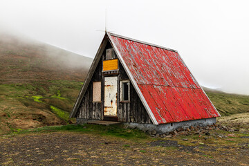 Old abandoned wooden hut with red roof standing on green hillside