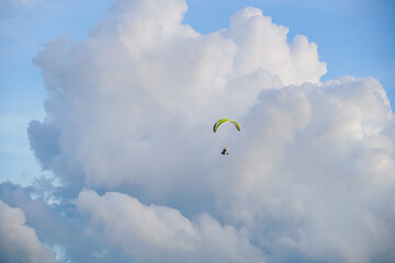 Paraglider with motor flying in the cloudy sky. Tiny cloud floating against the clear blue sky. Fly on paramotor On the blue sky and white clouds.