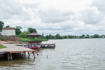 Wooden pier with gazebo on the lake. Country holiday, summer weekend.