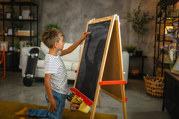 Young boy draw on blackboard whit chalk in the living room