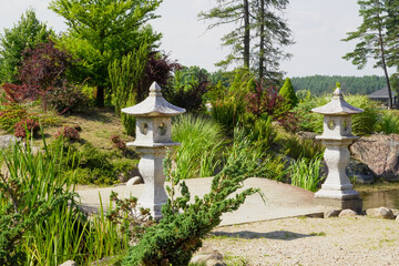 A peaceful Japanese garden scene featuring elegant stone lanterns surrounded by lush greenery and a calm pond, captured on a sunny day. Ideal for zen-themed projects