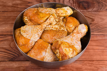 Raw chicken drumsticks with spices in bowl on rustic table