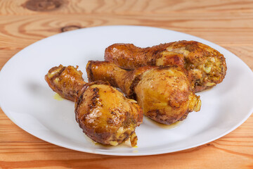 Baked chicken drumsticks on white dish, side view close-up