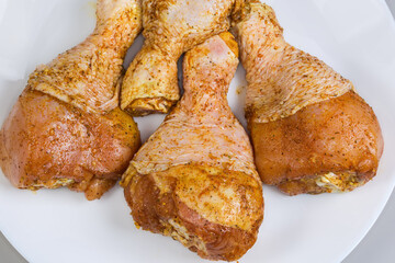 Raw chicken drumsticks with spices on dish, fragment close-up