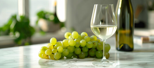 A glass of white wine sits on a marble countertop next to a bunch of green grapes, in a bright and airy kitchen setting