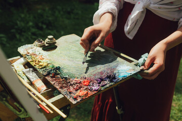 Close up of female artist's hands clear the palette of paints on the easel. Mindfulness, art therapy, creativity concept. Process of plein air painting in nature. Part of the series
