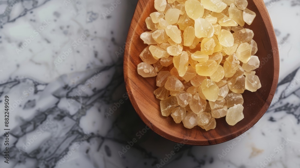 Poster  A wooden spoon holding yellow crystals on a white marble countertop, adjacent to another marbled surface