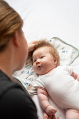 Caring young mother playing with her newborn baby daughter in the bed and looking at her with a smile, happy moments of maternity