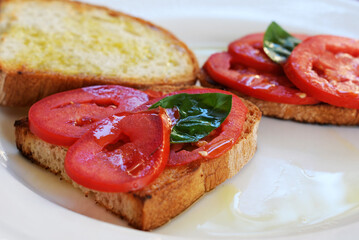 Italian crostini with slices of tomato, fresh basil leaves and olive oil on a white plate