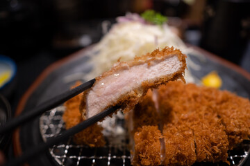 Chopsticks picking up a slice of Japanese deep-fried pork, or tonkatsu.