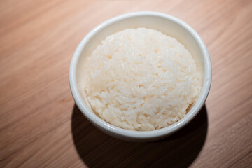 Bowl cooked rice in white ceramic bowl on a wooden table.