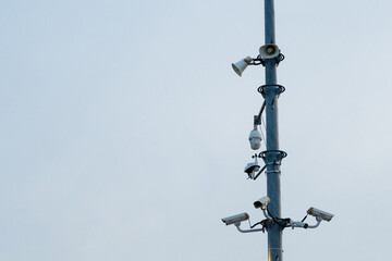 Different types of CCTV security cameras and loudspeakers installed on a pole in the city.