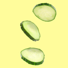 Fresh cucumber slices in air on yellow background