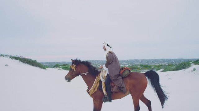A muslim riding his horse in the desert on a windy day