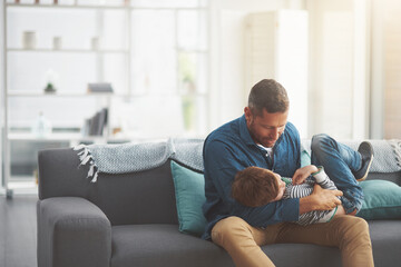 Obraz premium Father, boy and tickle kid on sofa together in home, bonding and hug for love in conversation. Daddy, son and family playing in living room for games, talk and embrace for security in relationship
