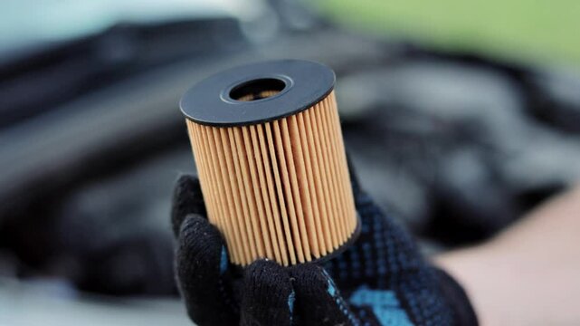 Auto mechanic holds an oil filter for gasoline cars in his hands in black gloves, close-up.