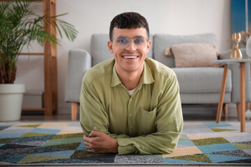 Fototapeta premium Handsome happy young man in new stylish eyeglasses lying on floor at home