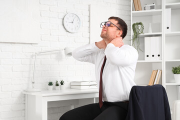 Businessman suffering from neck pain at table in office