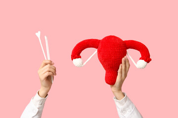 Doctor's hands with female uterus and pap test tools on pink background