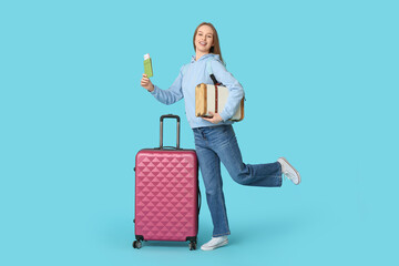 Smiling young woman with luggage, passport and ticket on blue background. Travel concept