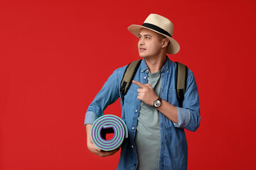 Young male tourist with travelling mat pointing at something on red background