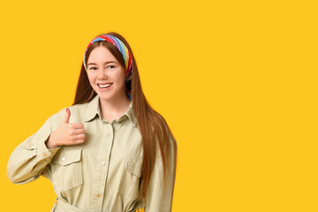 Fototapeta premium Success and approval concept, happy young woman showing thumbs up gesture with positive attitude and smiling expression on a bright yellow background