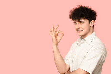 Smiling young man with dental braces showing OK on pink background