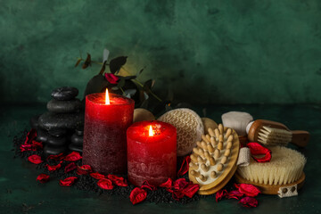 Glowing aroma candles with spa supplies on dark green background