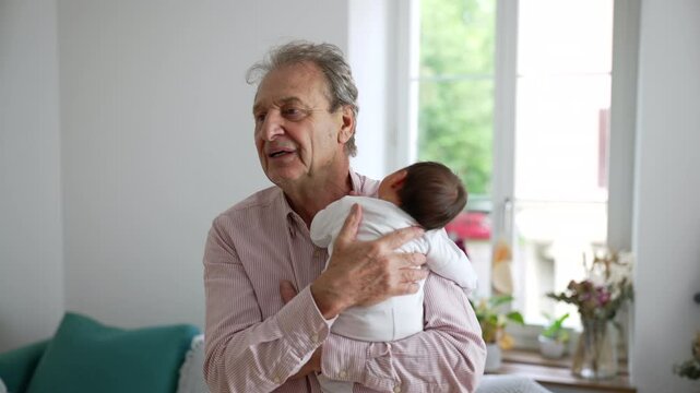 Grandfather looking lovingly at newborn baby, holding the infant close in a bright living room, showcasing the tender bond and affection between grandparent and grandchild