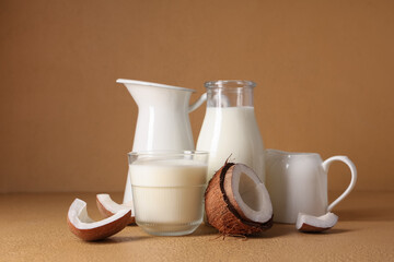 Glass, bottle and jugs of tasty fresh coconut milk on beige background