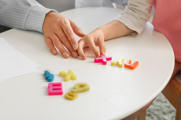 Female speech therapist working with little girl at table in office, closeup