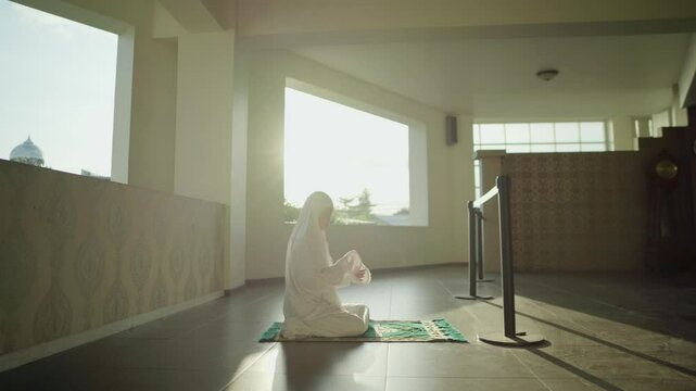 an asian muslim woman is raising her hands and praying to allah in the mosque in the afternoon. he increased his worship during the month of Ramadan