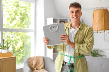 Young man with weight scales and tape measure at home