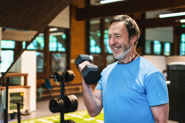 A man is smiling while lifting a pair of dumbbells. He is in a gym