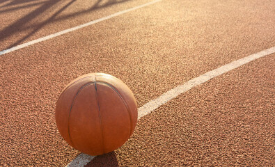 Basketball ball on the ground. Close-up ball on the red court. Basketball on the street or indoor court. Sports gear without people. Minimalism. Template, sport background 
