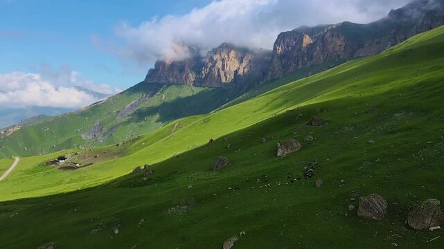 A green grasscovered mountain with a blue sky and clouds in the background