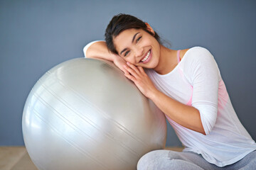 Fototapeta premium Fitness, happy woman and exercise ball in portrait on floor for core workout, balance and weight loss in studio. Yogi, smile and training equipment for health, wellness and cardio on grey background