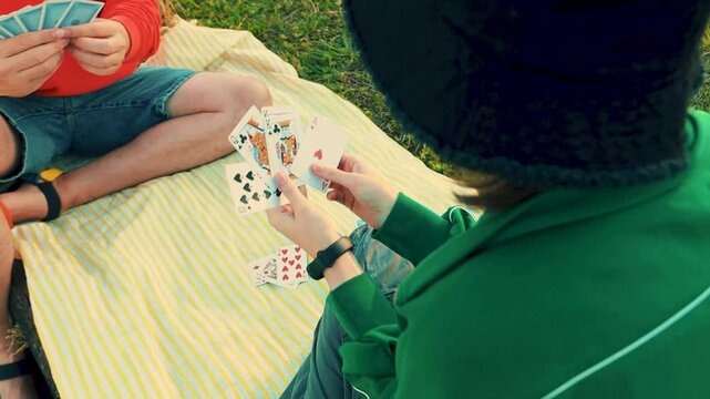 Smiling teenager girl playing card game with family. Creative outdoors leisure and education of kid. Family activity at the park.