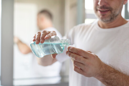 Man pouring blue mouthwash, for good dental health and fresh breath, closeup shot, focus on hands