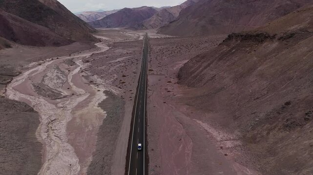 Aerial view of car driving across barren Atacama Desert Ojos del Salado volcano in distance. Aerial perspective of vehicle navigating through Atacama Desert near impressive Ojos del Salado volcano.