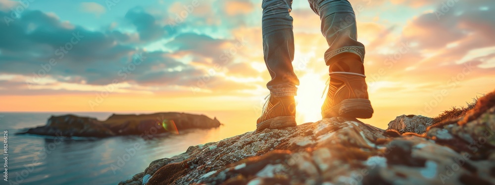 Wall mural a person is standing on a rocky cliff overlooking the ocean. the sky is a mix of blue and orange, cr