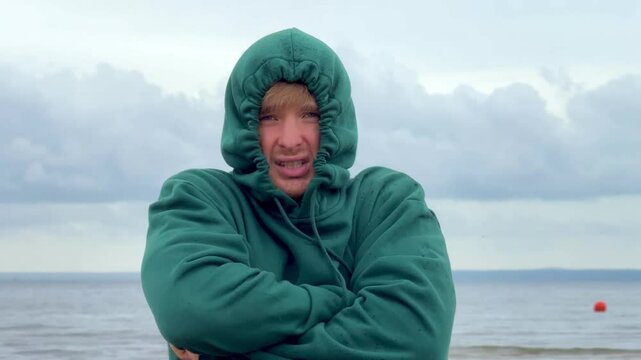 Sad upset man is suffering from cold, rain on the beach. Bad vacation.