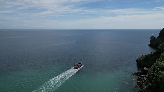 Babbacombe, South Devon, England: DRONE VIEWS: A tourist boat sails alongside the rugged coastline near Babbacombe. Babbacombe is a popular UK holiday destination renowned for its beautiful views.