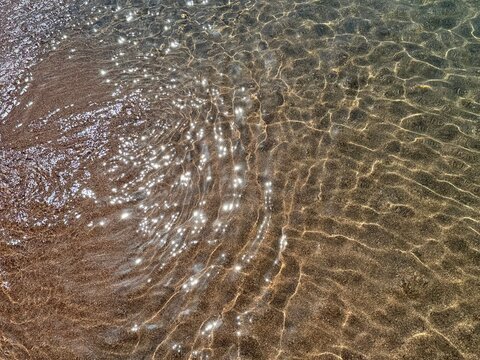 Clear sea water with sun light reflections on sandy beach