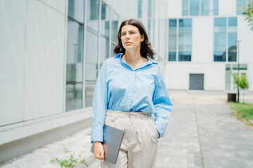 One beautiful young successful business woman going to work at business office modern building while holding laptop and wearing glasses	