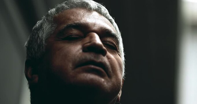 Unshavel contemplative senior man closes eyes in quiet meditation amidst problems wanting calm and peace during challenging times, close-up face