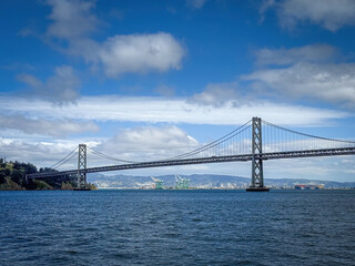Scenic view of San Francisco-Oakland Bay Bridge and Oakland with container terminal in the background, California, USA seen from the water against blue sky with clouds