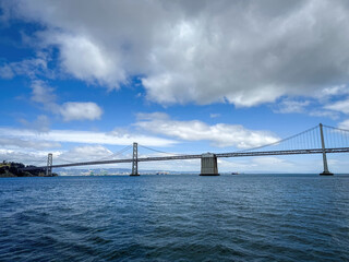 Scenic view of San Francisco-Oakland Bay Bridge and Oakland with container terminal in the background, California, USA seen from the water against blue sky with clouds