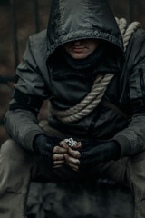 A man in a gas mask and camouflage sits on the ruins with a flower in his dirty hands. The concept of hope for a bright future after the war or memories of the past.