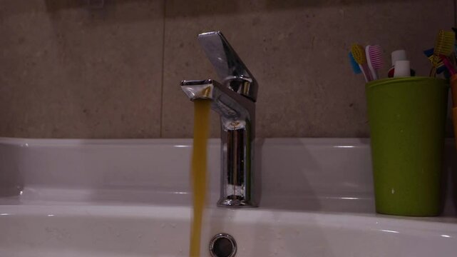 Dirty rusty water flowing from the home kitchen tap after the human hand turns on the faucet. Contamination water problem. Faucet water pollution. 4K